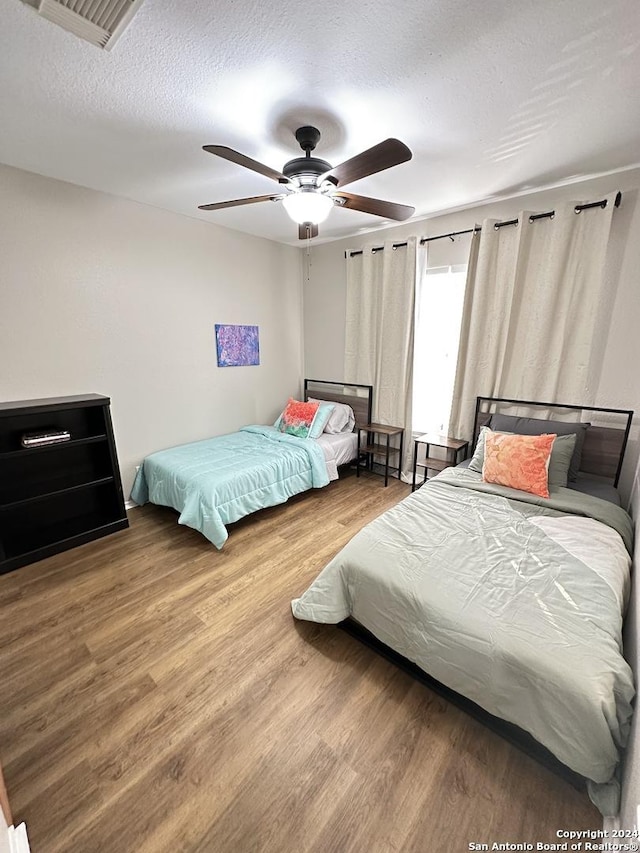 bedroom featuring a ceiling fan, a textured ceiling, visible vents, and wood finished floors