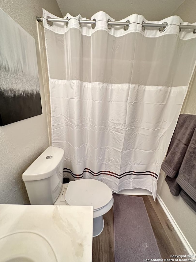 full bathroom with a shower with shower curtain, a textured wall, toilet, and wood finished floors