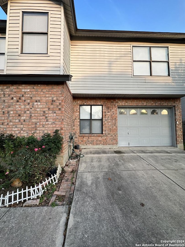 view of front of home featuring a garage, concrete driveway, brick siding, and fence