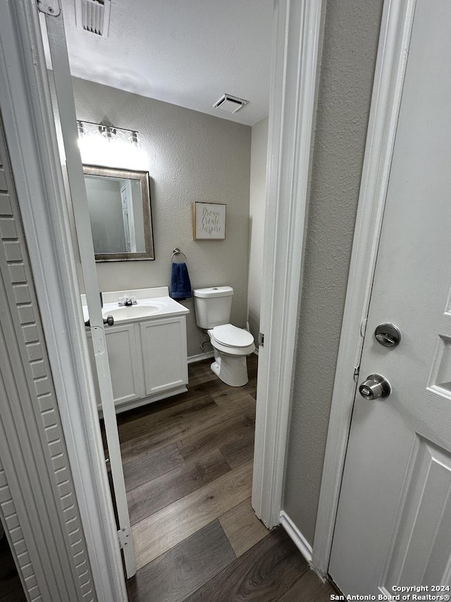 half bathroom with visible vents, a textured wall, toilet, vanity, and wood finished floors