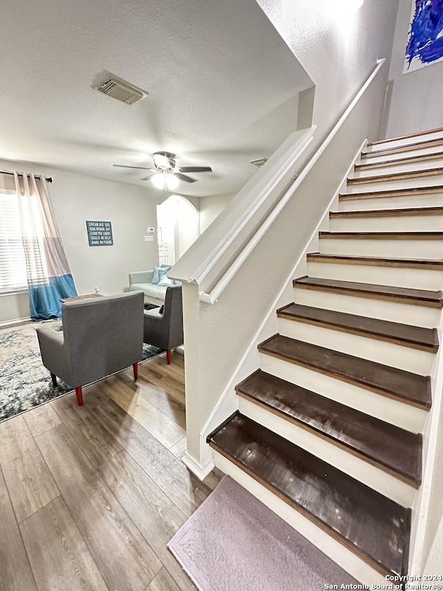 stairway featuring ceiling fan, a textured ceiling, visible vents, and wood finished floors