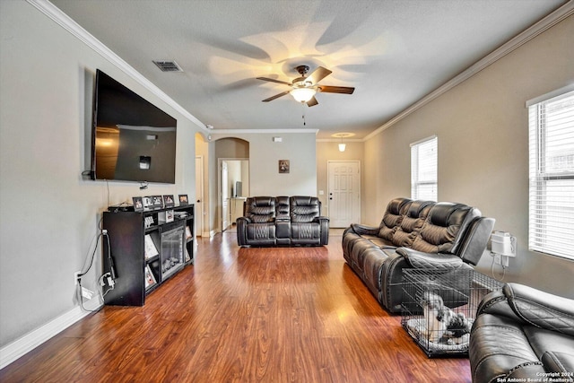 living room featuring visible vents, arched walkways, a ceiling fan, ornamental molding, and wood finished floors