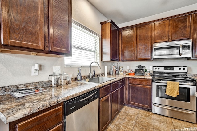 kitchen with sink, stainless steel appliances, light tile patterned flooring, and stone countertops