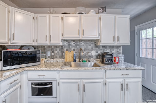 kitchen featuring light stone counters, sink, decorative backsplash, and white cabinets