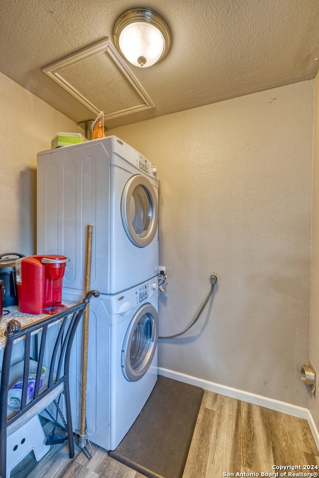 laundry room with a textured ceiling, stacked washer / drying machine, and hardwood / wood-style flooring