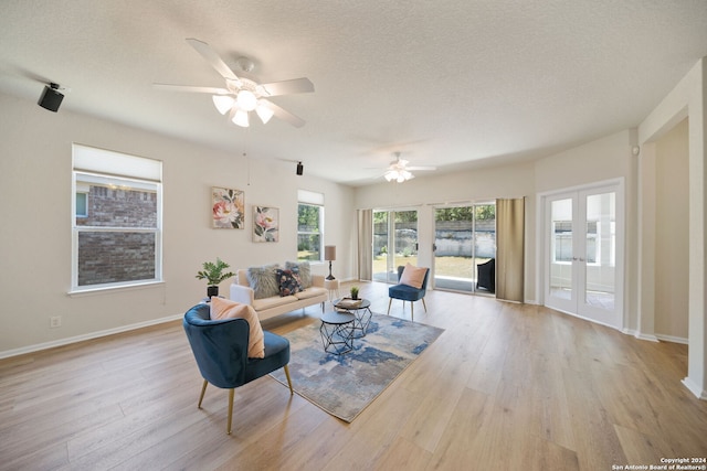 living room with light wood-type flooring, ceiling fan, and a textured ceiling