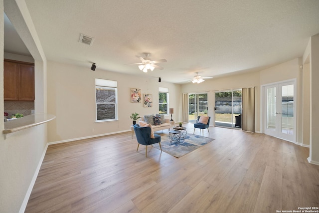 living room with ceiling fan, a textured ceiling, and light hardwood / wood-style flooring