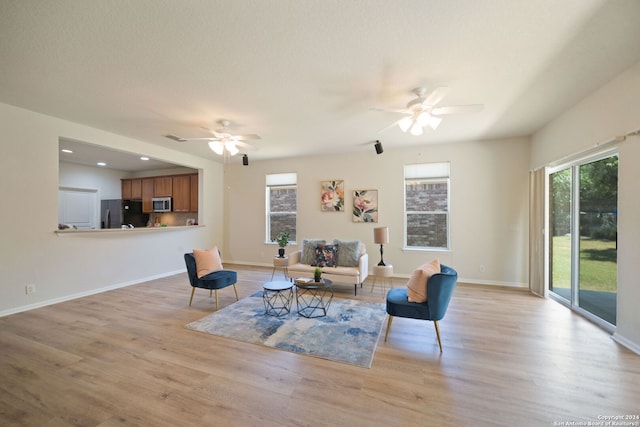 living room with light wood-type flooring, ceiling fan, and a textured ceiling