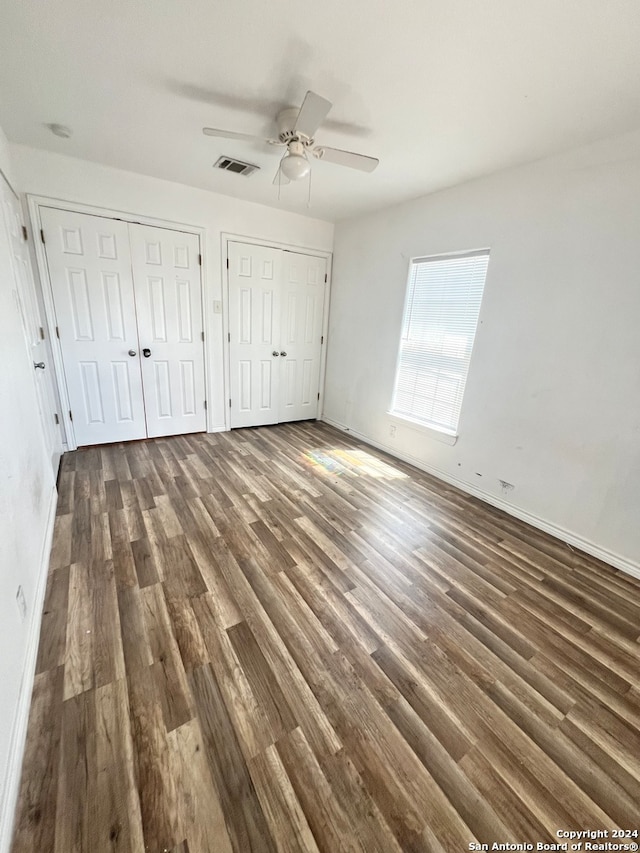 unfurnished bedroom with baseboards, visible vents, dark wood finished floors, ceiling fan, and multiple closets