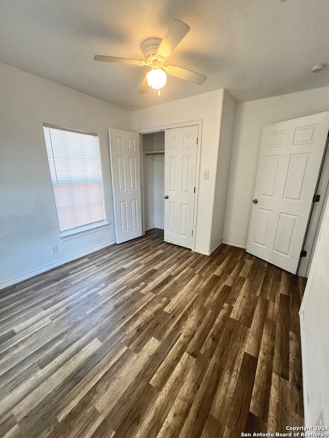 unfurnished bedroom with dark wood-style floors, a closet, baseboards, and a ceiling fan