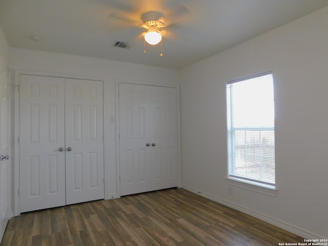 unfurnished bedroom featuring dark wood-style flooring, multiple closets, visible vents, ceiling fan, and baseboards