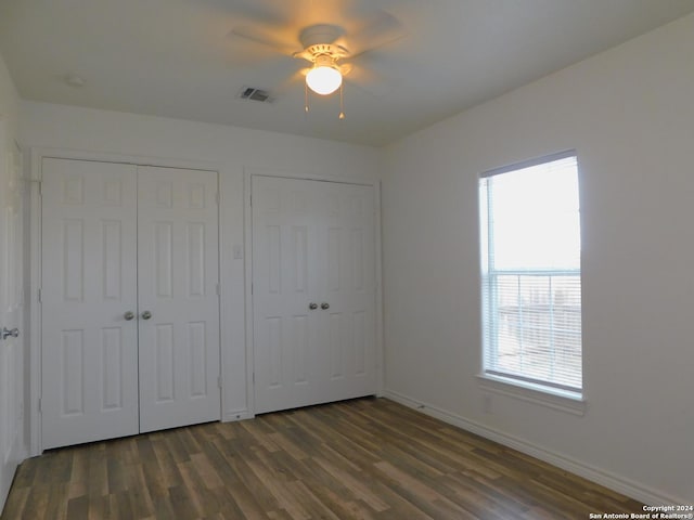 unfurnished bedroom featuring dark wood-style floors, baseboards, visible vents, and two closets