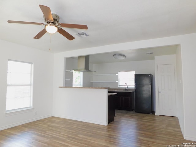 kitchen featuring a peninsula, a healthy amount of sunlight, light countertops, wall chimney range hood, and freestanding refrigerator