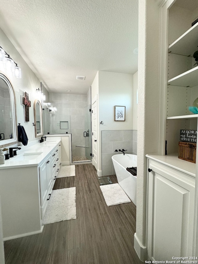 bathroom with tile walls, independent shower and bath, wood-type flooring, vanity, and a textured ceiling