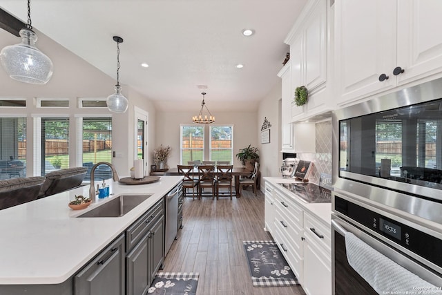 kitchen with white cabinetry, sink, decorative light fixtures, and a center island with sink