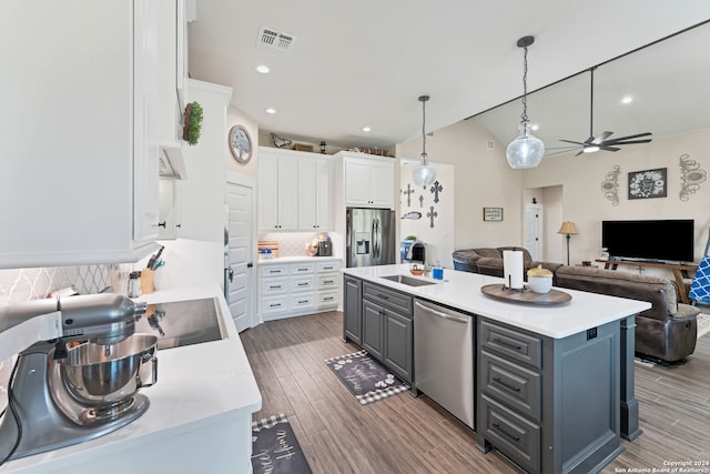 kitchen with appliances with stainless steel finishes, white cabinetry, pendant lighting, decorative backsplash, and a kitchen island with sink