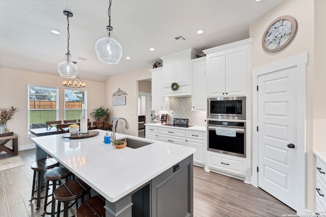 kitchen with an island with sink, appliances with stainless steel finishes, sink, and white cabinets