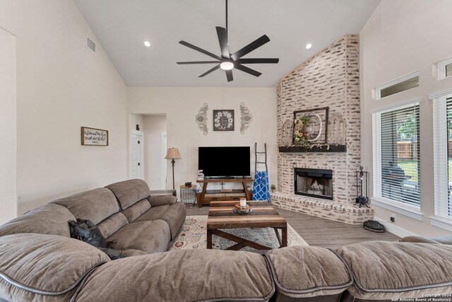 living room with ceiling fan, high vaulted ceiling, hardwood / wood-style floors, and a brick fireplace