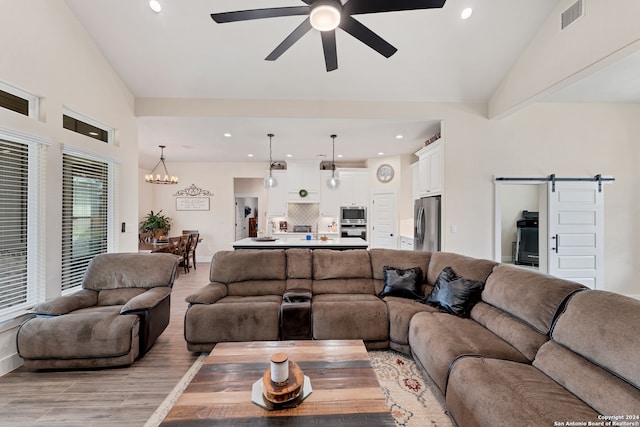 living room featuring high vaulted ceiling, a barn door, ceiling fan with notable chandelier, and light wood-type flooring