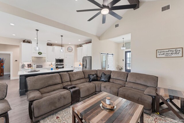 living room featuring high vaulted ceiling, light wood-type flooring, beamed ceiling, ceiling fan, and a barn door