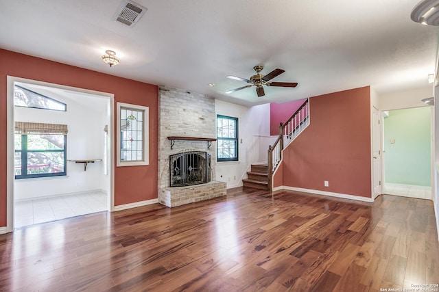 unfurnished living room with ceiling fan, a fireplace, wood finished floors, visible vents, and stairs