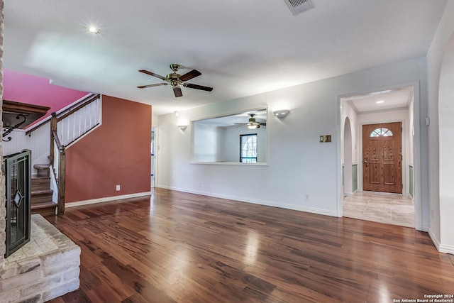 unfurnished living room with arched walkways, dark wood-type flooring, stairway, and visible vents