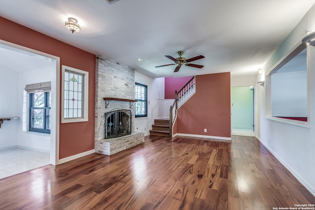 unfurnished living room featuring ceiling fan, hardwood / wood-style flooring, a textured ceiling, and a brick fireplace