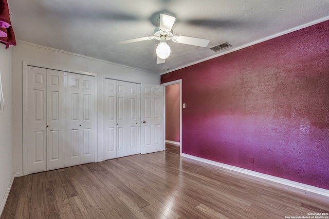 unfurnished bedroom with ceiling fan, crown molding, hardwood / wood-style flooring, and two closets