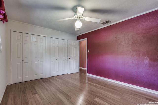 unfurnished bedroom featuring multiple closets, visible vents, ornamental molding, and light wood finished floors