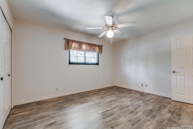 unfurnished bedroom featuring ceiling fan, wood finished floors, baseboards, a closet, and crown molding