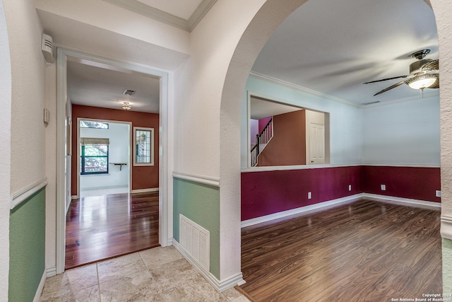 empty room featuring arched walkways, crown molding, visible vents, a ceiling fan, and wood finished floors