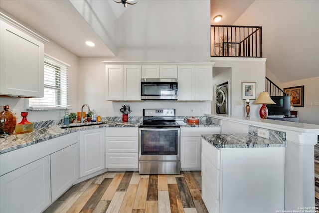 kitchen featuring appliances with stainless steel finishes, washer / dryer, kitchen peninsula, and white cabinets