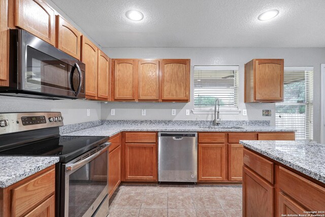 kitchen with appliances with stainless steel finishes, sink, light stone countertops, a textured ceiling, and light tile patterned floors