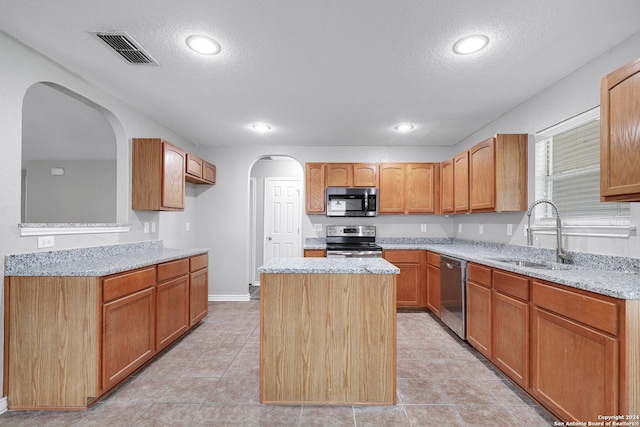 kitchen with appliances with stainless steel finishes, a kitchen island, light tile patterned floors, and light stone countertops