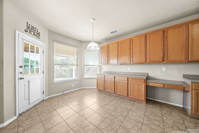 kitchen featuring brown cabinets, built in study area, visible vents, and decorative light fixtures