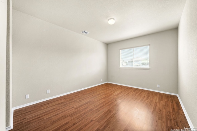 empty room with baseboards, visible vents, and wood finished floors