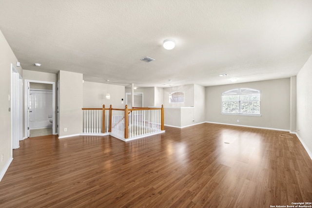 empty room featuring a textured ceiling, baseboards, and dark wood-type flooring