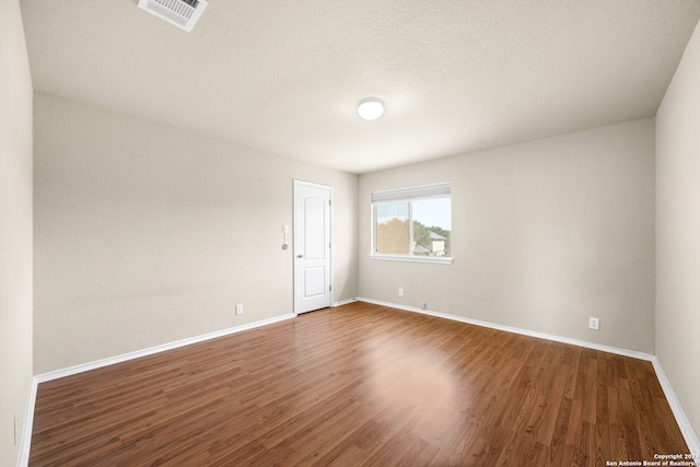 empty room with a textured ceiling, wood finished floors, visible vents, and baseboards