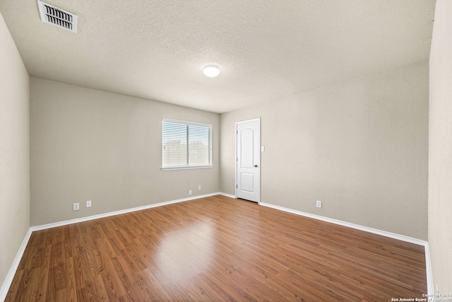 unfurnished room with a textured ceiling, wood finished floors, visible vents, and baseboards