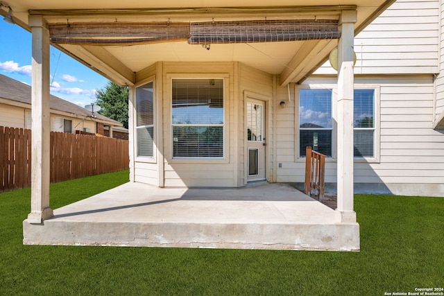 view of exterior entry with a lawn, a patio area, and fence