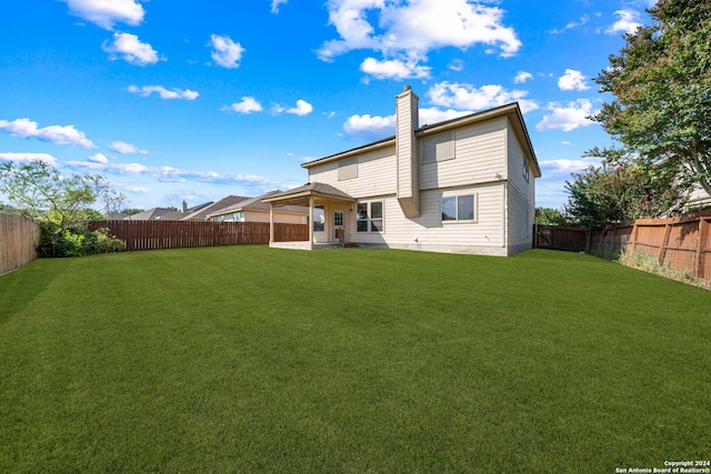 back of house with a chimney, a fenced backyard, and a lawn