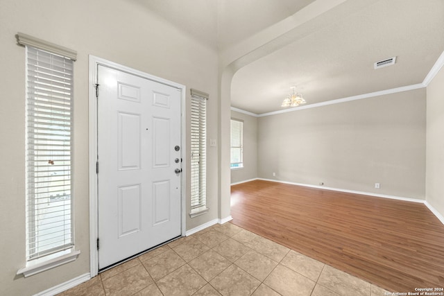 entrance foyer with arched walkways, ornamental molding, light tile patterned flooring, and baseboards