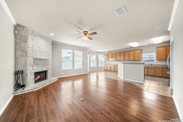 unfurnished living room featuring ceiling fan, a fireplace, visible vents, and light wood-style floors