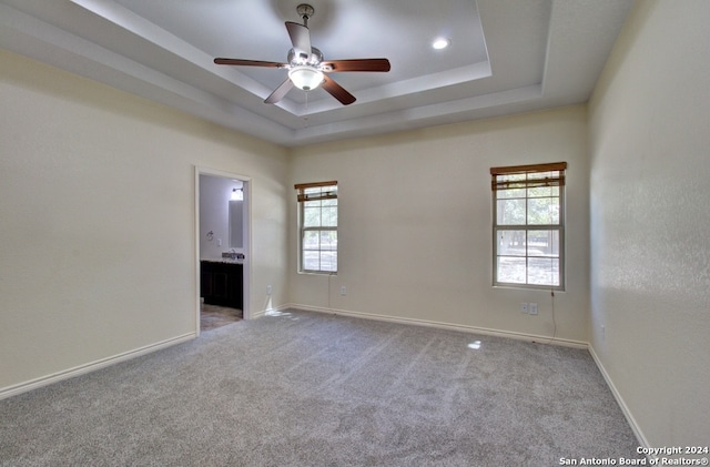 empty room with ceiling fan, a raised ceiling, and carpet