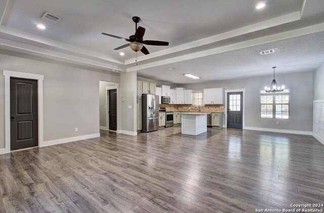 unfurnished living room with hardwood / wood-style flooring, a raised ceiling, and ceiling fan with notable chandelier