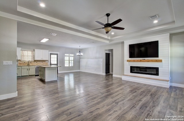 unfurnished living room featuring hardwood / wood-style flooring, a fireplace, a raised ceiling, and ceiling fan with notable chandelier