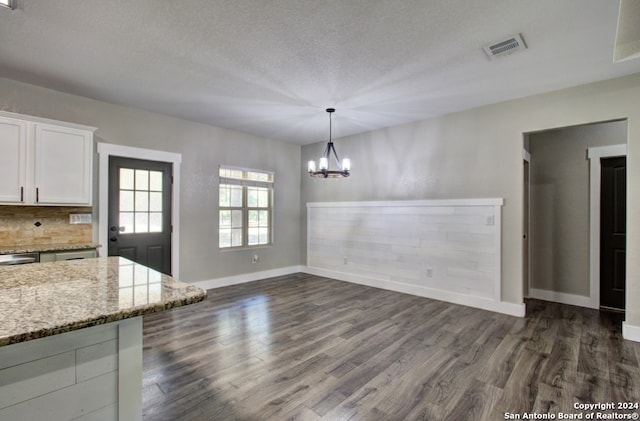 unfurnished dining area featuring a textured ceiling, an inviting chandelier, and dark wood-type flooring