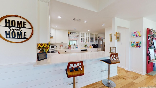 kitchen featuring a breakfast bar, sink, light hardwood / wood-style floors, white cabinetry, and kitchen peninsula