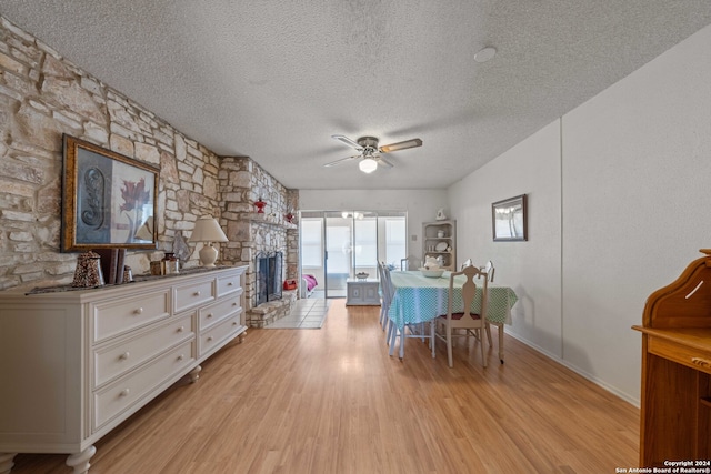 dining space featuring a textured ceiling, light hardwood / wood-style flooring, ceiling fan, and a stone fireplace