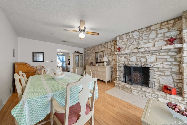 dining area with ceiling fan, a fireplace, a textured ceiling, and light hardwood / wood-style flooring